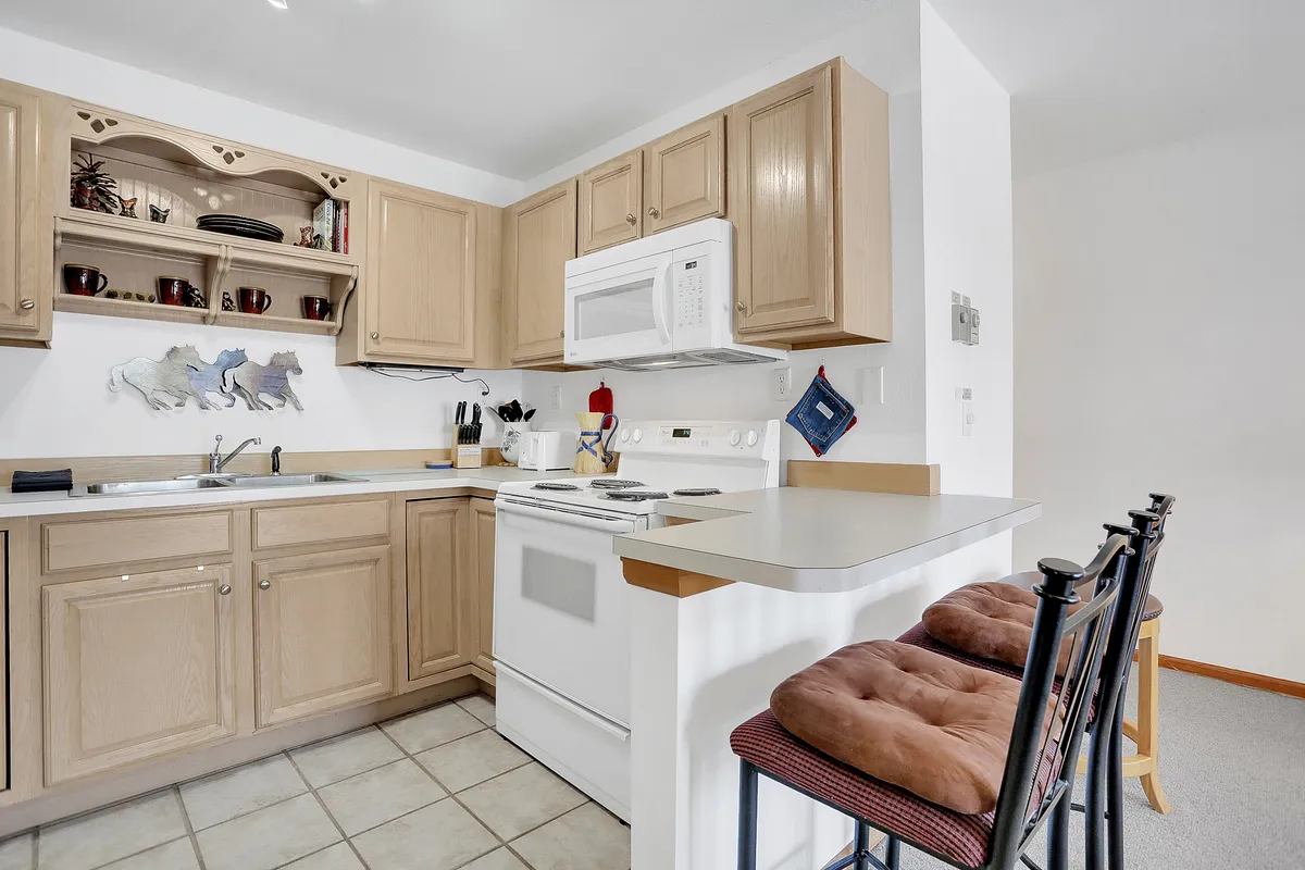 A cozy kitchen area featuring ample cabinetry, a modern stove, bar stools at a breakfast counter, and a well-lit sink. The setup highlights both practical cooking amenities and areas for informal dining or conversation, reinforcing the theme of togetherness.