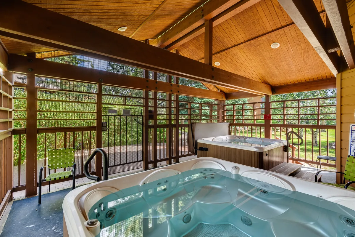 This image features inviting community hot tubs with wooden beams overhead and an outdoor view, suggesting a tranquil space to unwind. The setting allows for socializing with friends or quiet relaxation while enjoying nature.