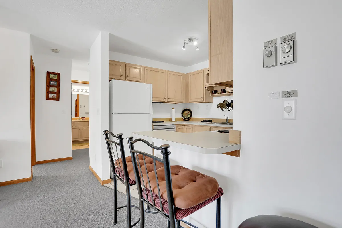 A spacious kitchen with a central island, surrounded by wooden cabinetry and bar stools. The island invites guests to gather, whether for meal prep, casual dining, or sharing stories. Warm lighting and open sightlines suggest the kitchen connects seamlessly to other living spaces.