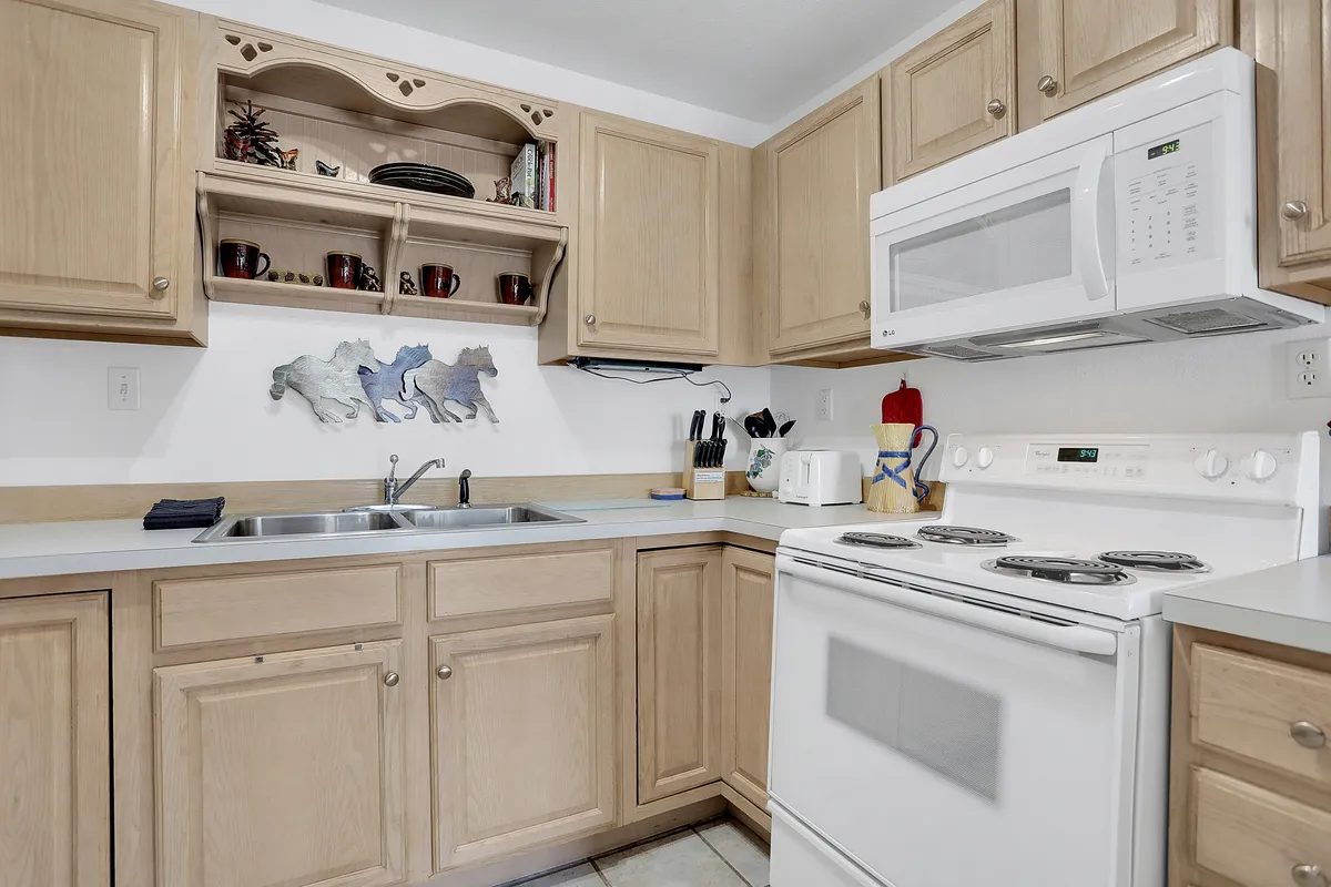A warm, homey kitchen with upper and lower cabinets, a stove, microwave, sink, and a decorative open shelf. The layout is designed for functionality and comfort, inviting guests to cook, bake, or simply enjoy a morning coffee at the counter.