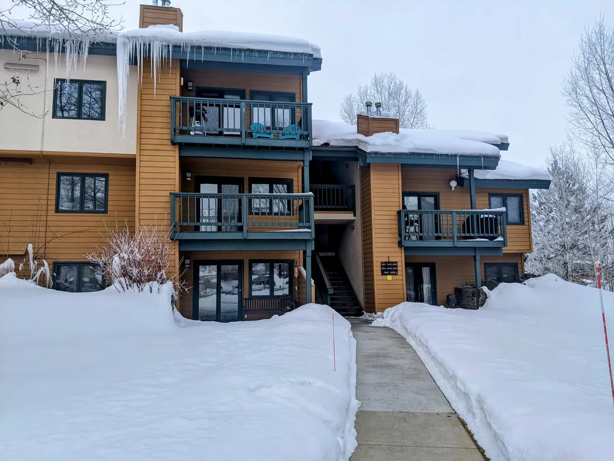 This image captures the exterior of a snow-covered building with welcoming balconies, icicles hanging from the roof, and a pathway leading toward the entrance. The surrounding area is blanketed in snow, creating a picturesque winter atmosphere.