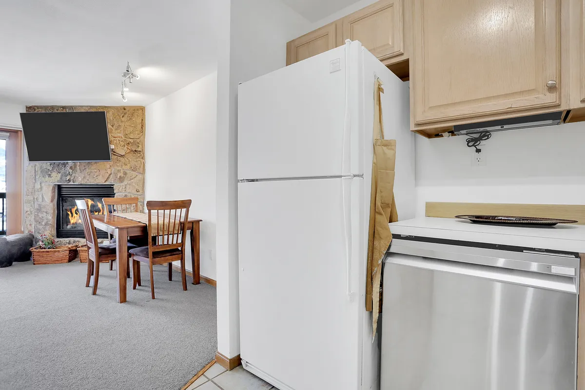 A comfortable open-plan space featuring a fireplace, dining table, and kitchen appliances in the background. The area is arranged for family dinners, game nights, and quiet evenings, with the fireplace as a focal point.