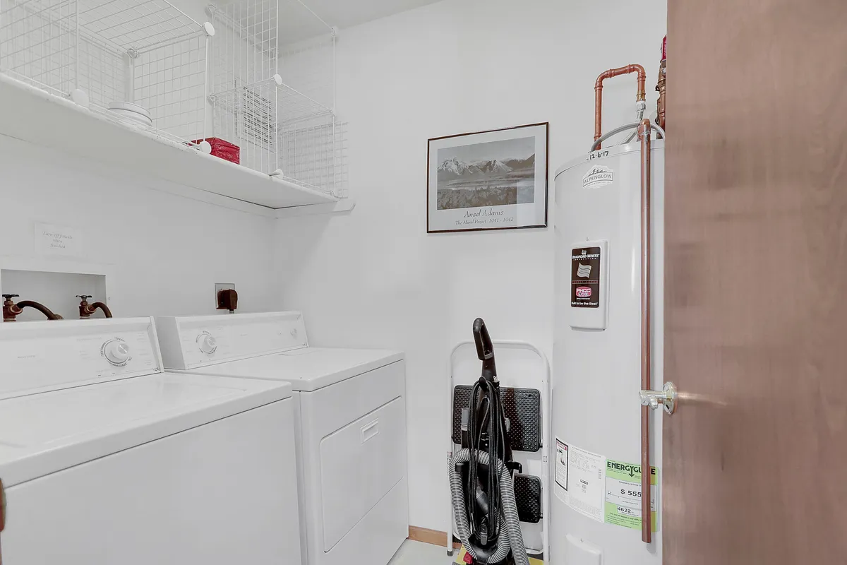 A well-organized laundry room with washing machine, dryer, shelving with baskets, a framed picture, and water heater. The setup is practical and assures guests of long-stay convenience.