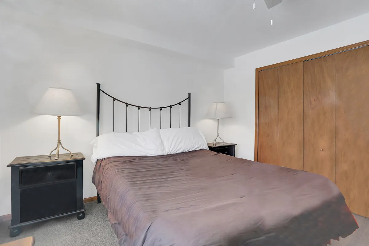 This image features a serene bedroom space with a queen bed flanked by nightstands and lamps, along with a closet. The inviting setup suggests comfort, peace, and relaxation, ideal for unwinding after an active day.