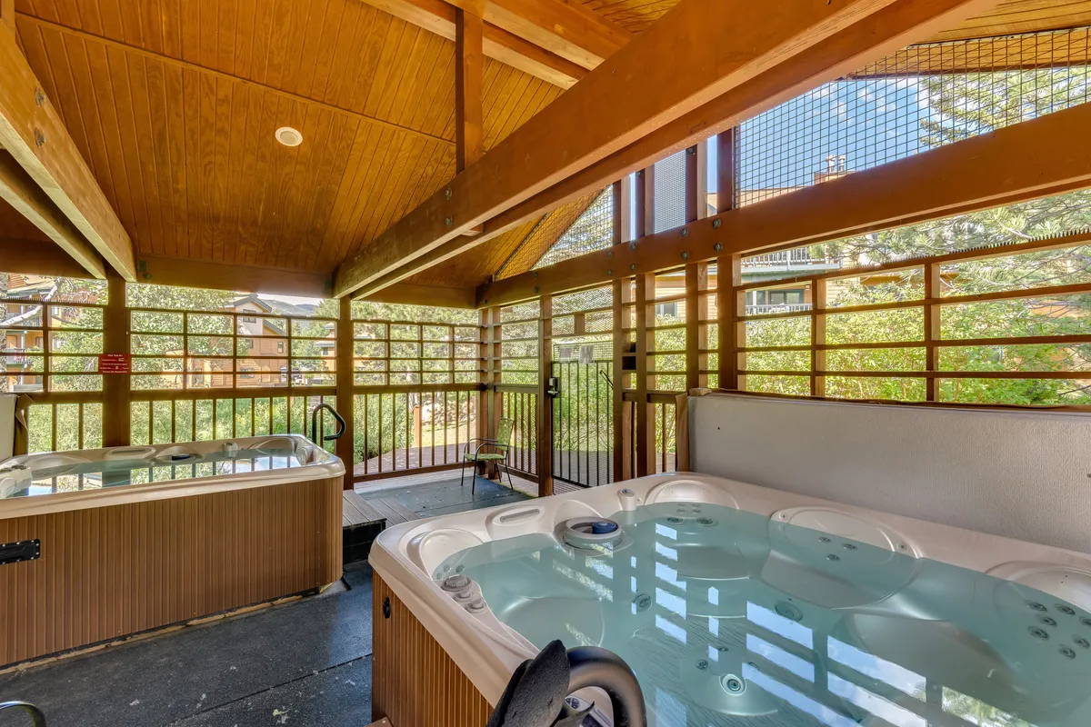 A tranquil interior space featuring inviting hot tubs framed by wooden beams and large windows that look out to nature. The image conveys relaxation and rejuvenation after a day spent outdoors.